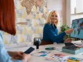 Uśmiechnięta pracownica biura podróży pokazuje na mapie świata na monitorze, jak zarabia się w biurze podróży.