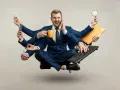 Biznesmen z wieloma rękami, przytłoczony nadmierną kontrolą w pracy, trzyma kubek kawy, telefon, żarówkę, lupę, klawiaturę i długopis.