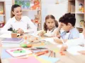 Uśmiechnięta nauczycielka przedszkola z dziećmi przy stoliku, tworząc inspirujący list motywacyjny dla przyszłych pedagogów.
