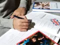 Osoba pisze ćwiczenia z angielskiego, obok leży książka i flaga Wielkiej Brytanii. Klauzula CV po angielsku może być częścią takich materiałów.