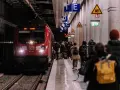 Pasażerowie czekają na czerwony pociąg DB na peronie. Zastanawiasz się, ile zarabia konduktor PKP?