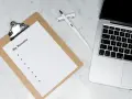 Na biurku leży laptop, notatnik z napisem "My Resume" i długopis. Czas przygotować CV, uwzględniając stopnie naukowe po angielsku.