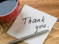 Na serwetce napisano "Thank you". Obok filiżanka kawy i długopis. To jak mail na pożegnanie w pracy.