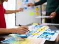 Zespół projektuje interfejsy, analizując potencjalne ux designer zarobki. Na stole makiety, palety kolorów i laptop.