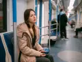 Zmęczona podróżą w metrze, młoda kobieta z telefonem w dłoni. Może to znak, że potrzebuje L4 z powodu wypalenia zawodowego.