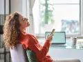 Kobieta z kręconymi włosami śmieje się, trzymając telefon. Może to być jej urlop na poszukiwanie pracy, pełen nadziei i pozytywnych wiadomości.