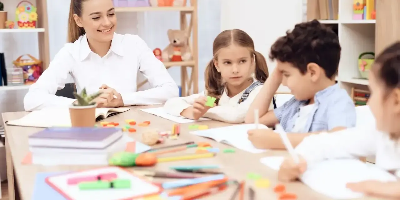 Uśmiechnięta nauczycielka przedszkola z dziećmi przy stoliku, tworząc inspirujący list motywacyjny dla przyszłych pedagogów.