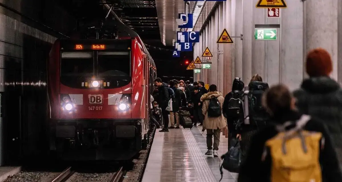 Pasażerowie czekają na czerwony pociąg DB na peronie. Zastanawiasz się, ile zarabia konduktor PKP?