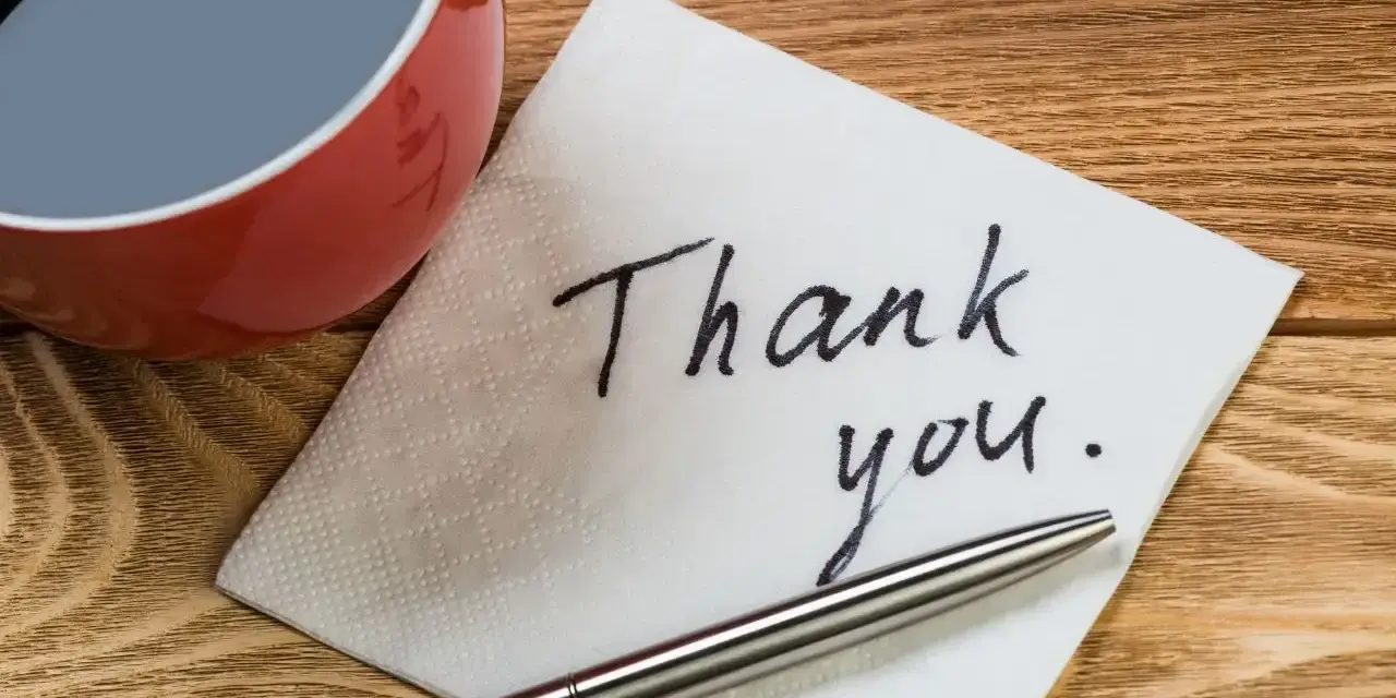 Na serwetce napisano "Thank you". Obok filiżanka kawy i długopis. To jak mail na pożegnanie w pracy.
