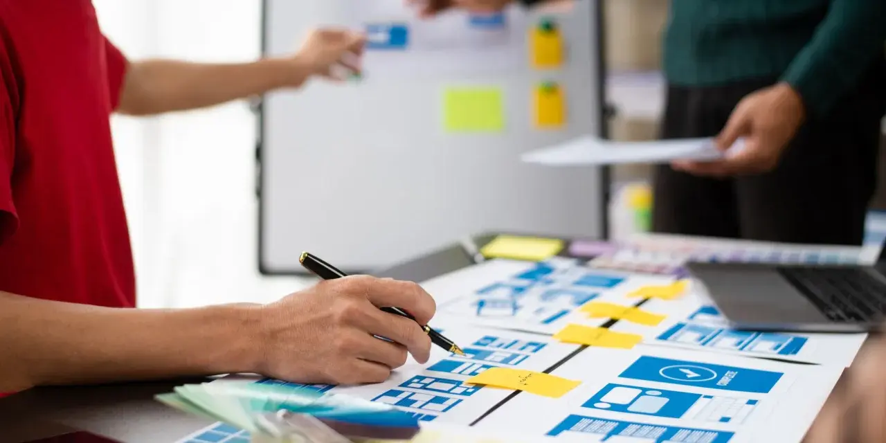 Zespół projektuje interfejsy, analizując potencjalne ux designer zarobki. Na stole makiety, palety kolorów i laptop.
