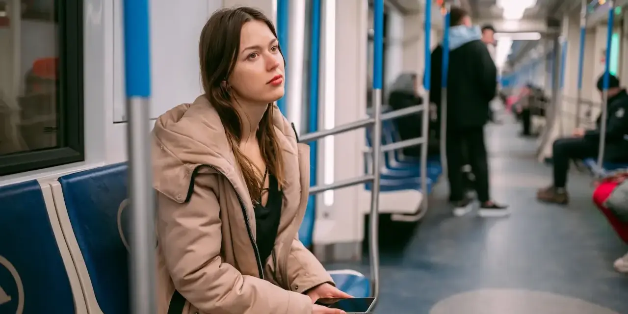 Zmęczona podróżą w metrze, młoda kobieta z telefonem w dłoni. Może to znak, że potrzebuje L4 z powodu wypalenia zawodowego.