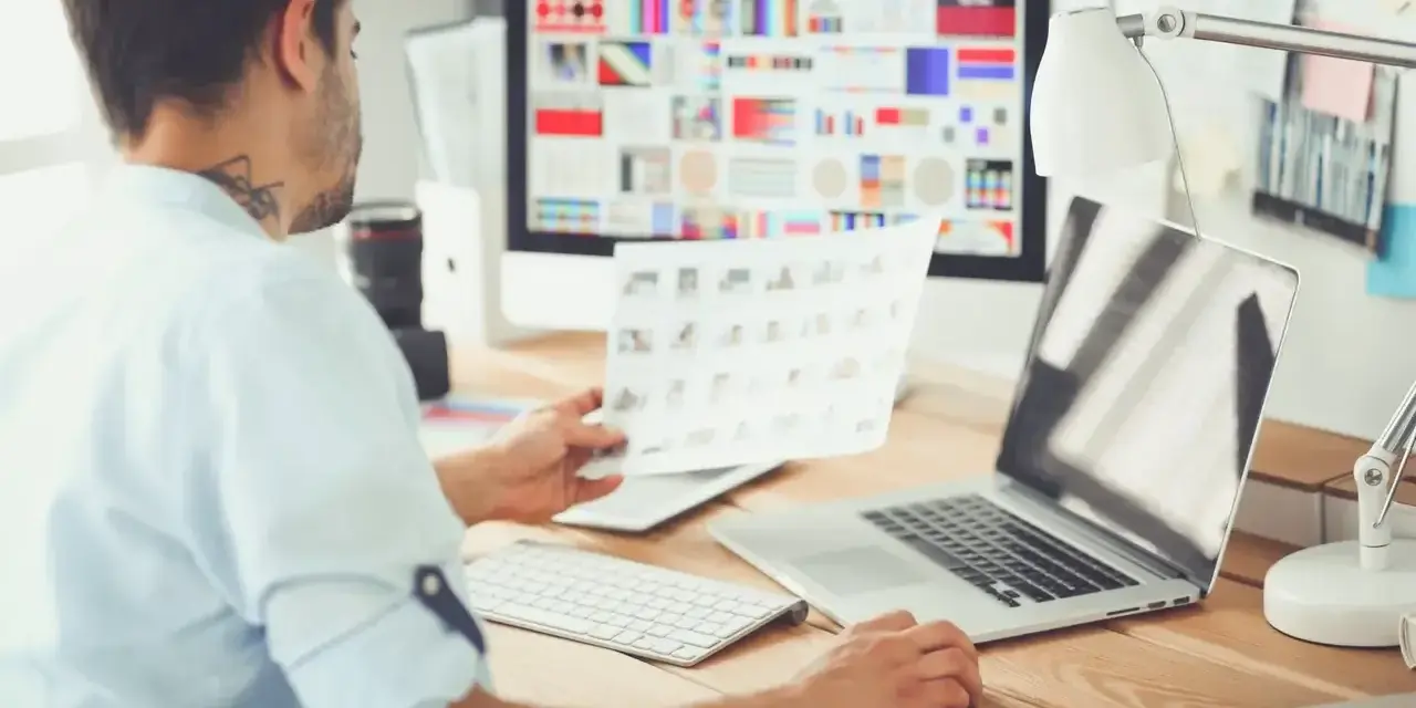 Mężczyzna, jako ux ui designer, analizuje wydruki z projektami na biurku.