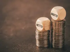 Dwie wieże monet, jedna z kostką "NETTO", druga z "BRUTTO". Symbolizuje to rozważania nad umową zlecenie i stawką godzinową.