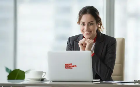 Uśmiechnięta kobieta z zapałem ogląda coś na laptopie z logo "New Heroes Academy". To znak, że jej zmiana zawodu jest na dobrej drodze.