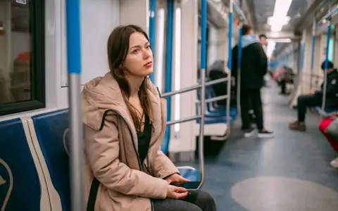 Zmęczona podróżą w metrze, młoda kobieta z telefonem w dłoni. Może to znak, że potrzebuje L4 z powodu wypalenia zawodowego.