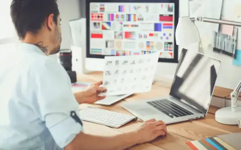 Mężczyzna, jako ux ui designer, analizuje wydruki z projektami na biurku.