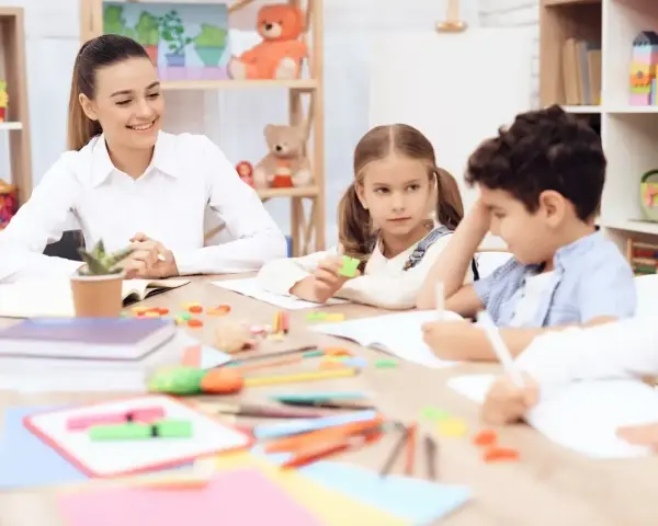 Uśmiechnięta nauczycielka przedszkola z dziećmi przy stoliku, tworząc inspirujący list motywacyjny dla przyszłych pedagogów.