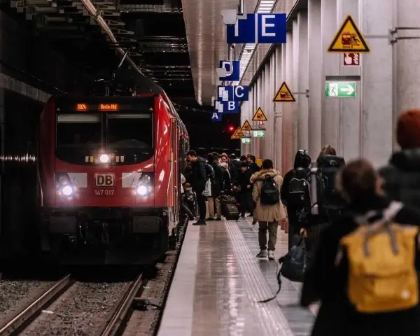 Pasażerowie czekają na czerwony pociąg DB na peronie. Zastanawiasz się, ile zarabia konduktor PKP?