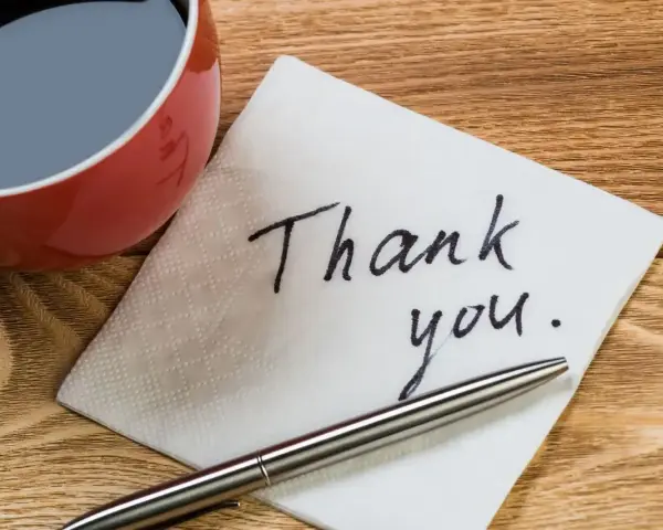 Na serwetce napisano "Thank you". Obok filiżanka kawy i długopis. To jak mail na pożegnanie w pracy.
