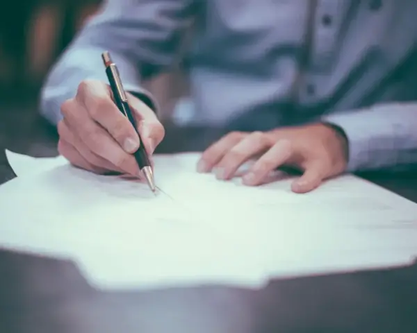 Dłoń pisze długopisem na papierze. Może to być wypowiedzenie umowy, a porzucenie pracy konsekwencje może mieć poważne.