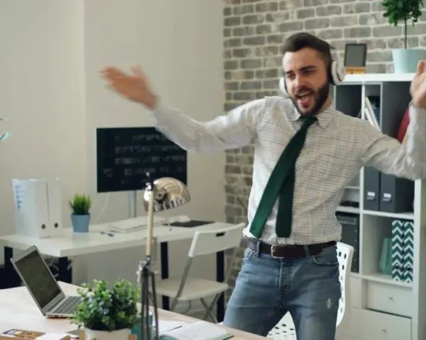 Szczęśliwy ENFP w pracy, tańczący w słuchawkach. W tle biuro z roślinami i komputerami.