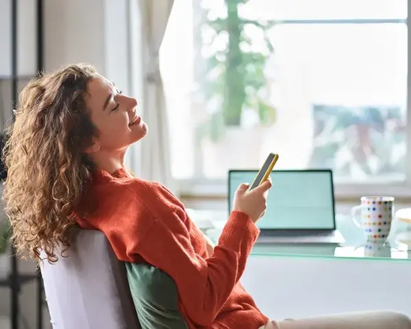 Kobieta z kręconymi włosami śmieje się, trzymając telefon. Może to być jej urlop na poszukiwanie pracy, pełen nadziei i pozytywnych wiadomości.