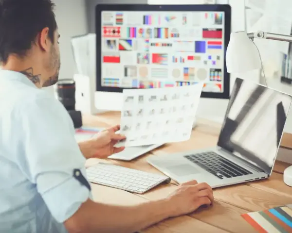 Mężczyzna, jako ux ui designer, analizuje wydruki z projektami na biurku.
