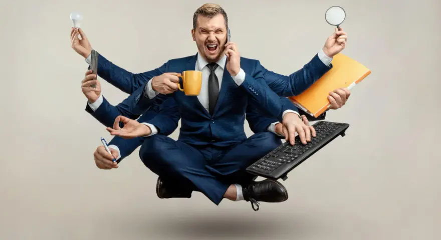 Biznesmen z wieloma rękami, przytłoczony nadmierną kontrolą w pracy, trzyma kubek kawy, telefon, żarówkę, lupę, klawiaturę i długopis.