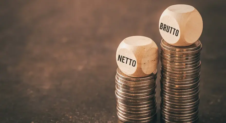 Dwie wieże monet, jedna z kostką "NETTO", druga z "BRUTTO". Symbolizuje to rozważania nad umową zlecenie i stawką godzinową.