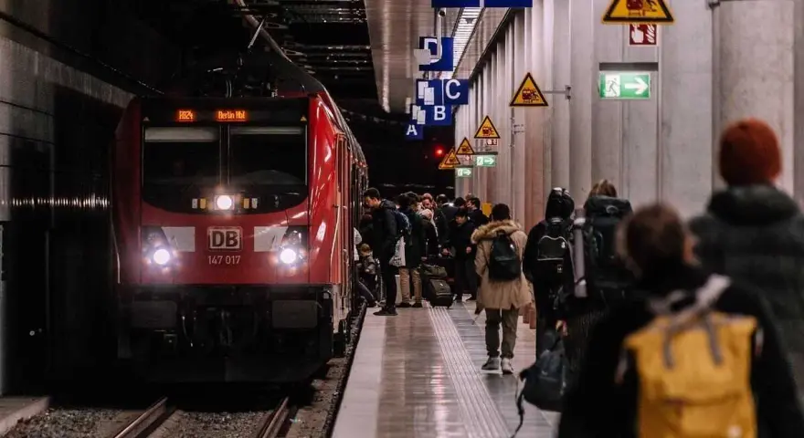 Pasażerowie czekają na czerwony pociąg DB na peronie. Zastanawiasz się, ile zarabia konduktor PKP?