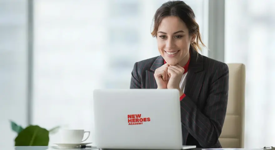Uśmiechnięta kobieta z zapałem ogląda coś na laptopie z logo "New Heroes Academy". To znak, że jej zmiana zawodu jest na dobrej drodze.