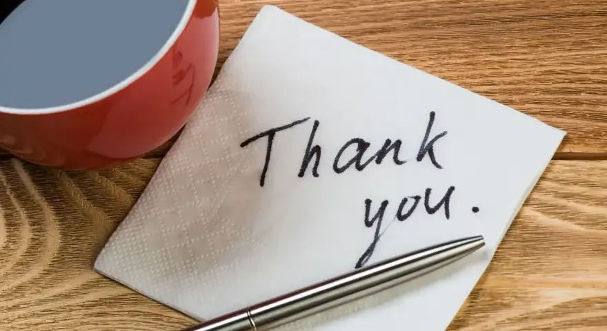 Na serwetce napisano "Thank you". Obok filiżanka kawy i długopis. To jak mail na pożegnanie w pracy.