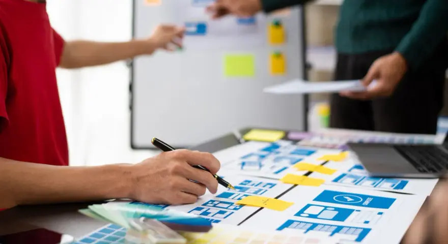 Zespół projektuje interfejsy, analizując potencjalne ux designer zarobki. Na stole makiety, palety kolorów i laptop.