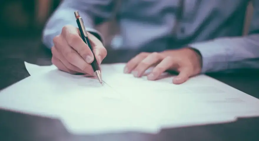 Dłoń pisze długopisem na papierze. Może to być wypowiedzenie umowy, a porzucenie pracy konsekwencje może mieć poważne.