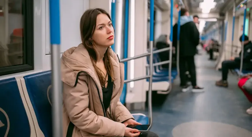 Zmęczona podróżą w metrze, młoda kobieta z telefonem w dłoni. Może to znak, że potrzebuje L4 z powodu wypalenia zawodowego.