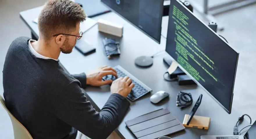 Mężczyzna w okularach pracuje przy komputerze, pisząc kod. To idealny obrazek dla CV front end developera.