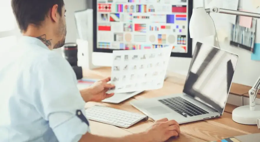Mężczyzna, jako ux ui designer, analizuje wydruki z projektami na biurku.