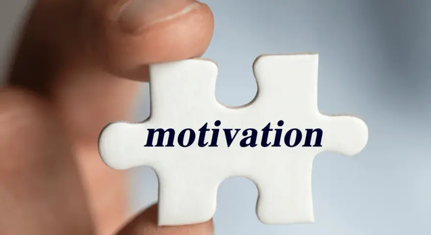 Palec trzyma element układanki z napisem "motivation". Klucz do sukcesu i tego, jak motywować pracowników, tkwi w znalezieniu właściwego elementu.