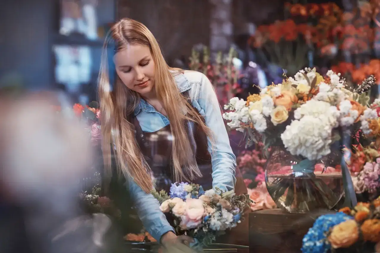 Blondynka w fartuchu tworzy bukiet, otoczona kwitnącymi kwiatami. Jej pasja do florystyki, jak u każdego INFP, przejawia się w delikatności i dbałości o detale.
